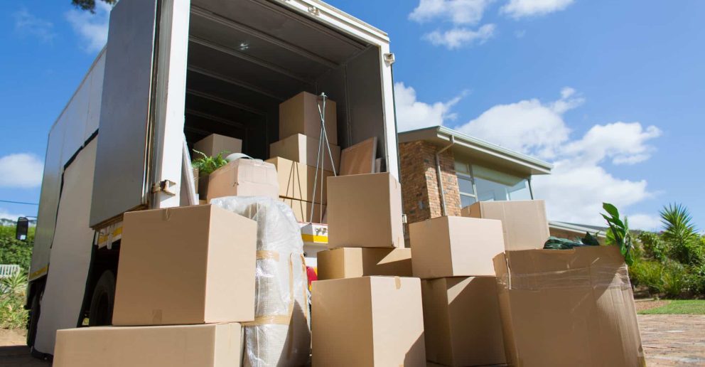 Cardboard boxes outside moving van and house in sunny driveway